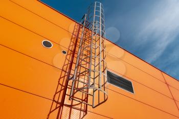 Orange industrial building wall with metal ladder,under blue sky