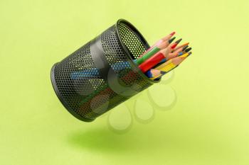 Colored pencils in a black mesh pen pot on a green background