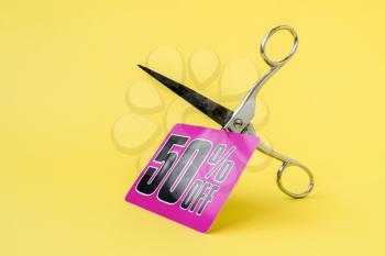 Metal scissors cutting the price tag on the yellow background. Cutting price or sale concept.
