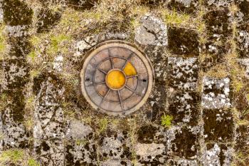 Old round iron manhole on the abandoned old tile with grass growing between the joints of the tile 