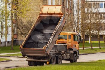 Tipper unloading fresh asphalt from body during road construction works