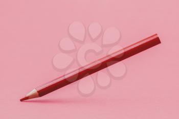 Red color pencil levitating over a pink background. Copy space.
