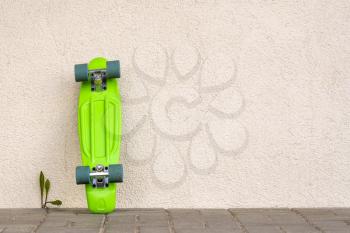 Green skateboard leaning against white wall. Copy space.