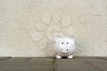 Piggy bank on the pavement against white wall. Copy space.