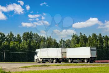 Road transport of goods by truck. White truck on an asphalt road in a rural landscape.