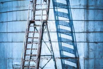 Ladder with access to a large tank in abandoned cargo terminal. Blue filtered image