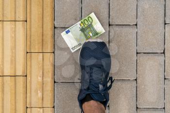 Money lying on the ground, shoe stepping on it. Euros lost on a street. 