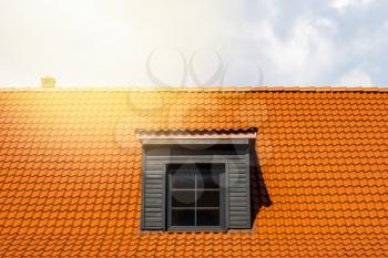 Renovated dormer window on the red clay ceramic tiles roof. Bright sunny day.
