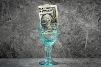 Wineglass with one dollar inside. The concept of alcoholism and a lot of money on alcohol.