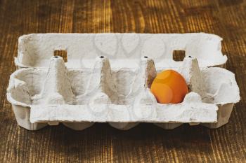One brown chicken egg in a cardboard box on a wooden background, close-up view