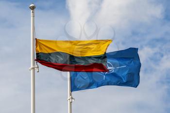 Lithuanian flag and NATO flag waving in the wind against sky background