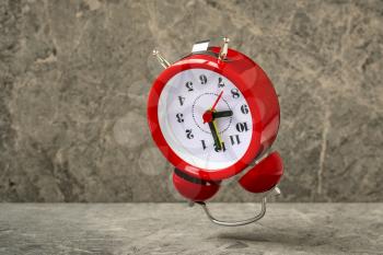 Red alarm clock falling on the stone background. Red alarm clock showing 9 o'clock in a morning.
