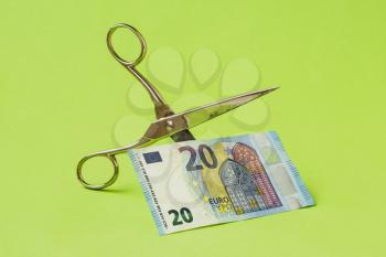 Cutting twenty Euro note with scissors on green background. Devaluation of Euro currency. 