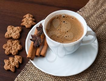 Coffee cup on sacking material with cinnamon stick and cookies