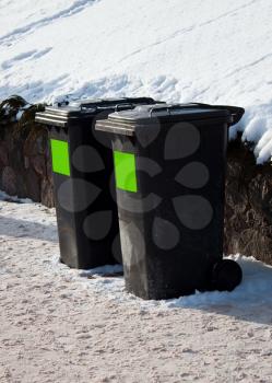 Two plastic trash containers in the winter steet