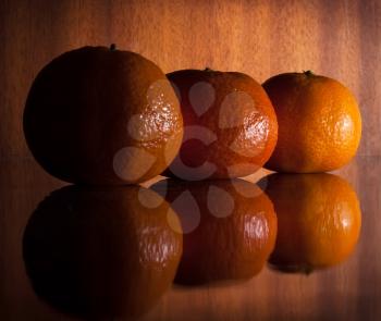 Three mandarines on the brown wooden background