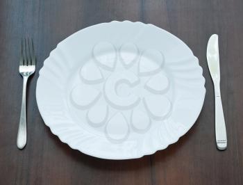 Ceramic plate with knife and fork on wooden background