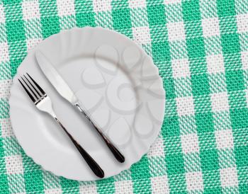 Plate with silverware on checquered green  background