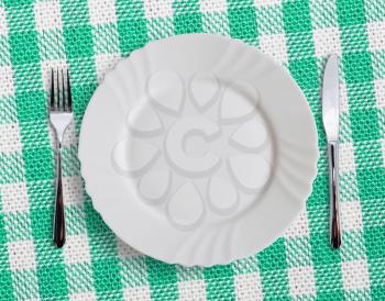 Plate with silverware on checquered green  background