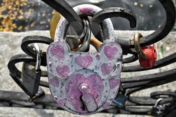 White with painted pink serrdechkami padlock close to the fence on the background of other castles, water, concrete fences