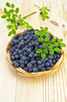 Blueberries in a wicker basket, two sprigs of blueberries with green leaves on a light wooden board