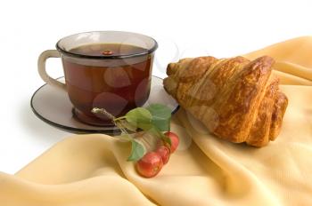 Brown glass cup with tea, croissant and wild apples on the beige light fabric isolated on a white background