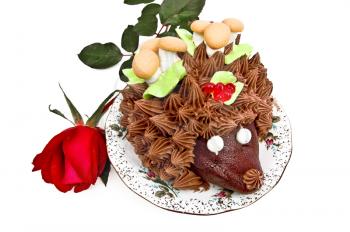 Cake in the form of a hedgehog, adorned with green leaves with cream, mushrooms from the biscuit and meringue, berries, jelly on a plate with a red rose bud