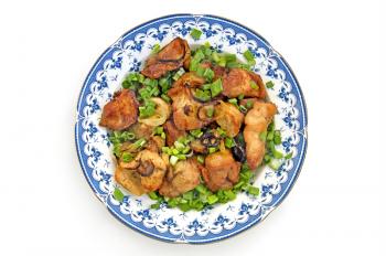 Chunks of roasted chicken with green onion in a dish is isolated on a white background