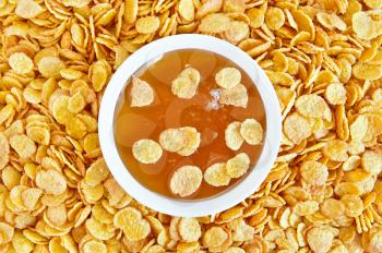 Honey in a white cup on the background texture of golden corn flakes