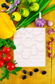 Lined sheet of paper small red and yellow tomatoes, yellow bell pepper, green onions, parsley, whole and two cloves garlic, black beans and kidney beans on a wooden board