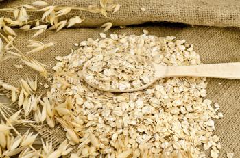 Oat flakes with a wooden spoon, stalks of oats on sacking and wooden board