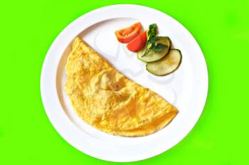 Yellow omelette, two slices of red tomato and cucumber, a sprig of parsley on a white plate isolated on green background