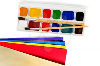 A box of paints, two brushes, color paper isolated on white background