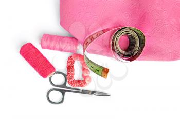 Two pink spool of thread, scissors, pink buttons, measuring tape, pink cloth isolated on a white background