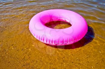 Pink childish lifebuoy against a background of golden sand and water