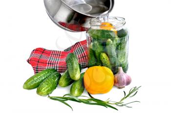 Cucumbers in a glass jar, yellow bell pepper, garlic, tarragon sprig, red and black checkered napkin, a pan with the brine is isolated on a white background
