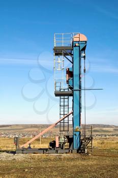 Vertical oil pump swing blue and red against a yellow-brown hills, villages and blue sky