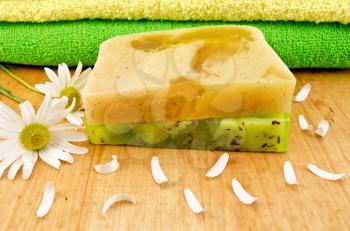 Homemade soap green and yellow, two towels, flowers and petals camomile against a wooden board