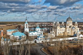 Snowy the Transfiguration Cathedral, beige Kresovozdvizhensky Cathedral with gray zinc domes, buildings, towers and walls of St. Nicholas Monastery against the blue sky and clouds (Verhoturie city of 