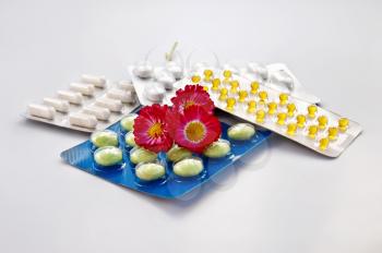 White and green pills, capsules yellow packages with three daisies isolated on gray background