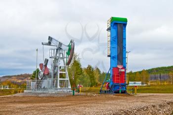 Vertical and horizontal oil pump against a yellow-green trees and a gloomy autumn sky