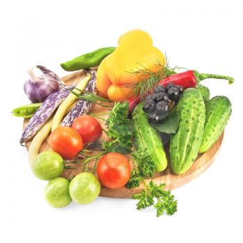 Tomatoes, cucumbers, sweet and hot peppers, pea pods, three pods of beans, garlic, parsley, dill, tarragon and brush Aronia on a wooden circular board isolated on white background