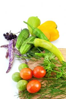 Tomatoes, two sharp pepper, parsley, dill, tarragon on a wooden board round, three cucumbers, two sweet peppers, three green beans, brush chokeberry isolated on a white background