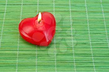 Red candle in the shape of a heart on a green bamboo mat