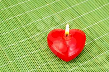 Red candle in the shape of a heart on a green bamboo mat in the bottom right corner