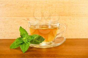 Herbal tea in a glass cup with a sprig of mint on the background of wooden boards