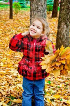Little girl with a bouquet of yellow maple leaves on a background of trees and yellow foliage