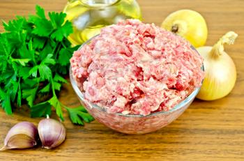 Minced meat in a glass bowl, parsley, onions, a bottle of vegetable oil, garlic on a wooden board
