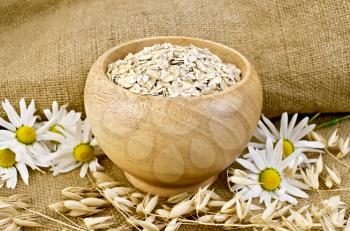 Oat flakes in a wooden bowl, stalks of oats, chamomile on burlap and wooden board