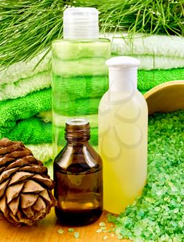 Cedar oil in a bottle, branch of cedar cones, towels and salt in a wooden bowl, lotion, shower gel on a wooden board